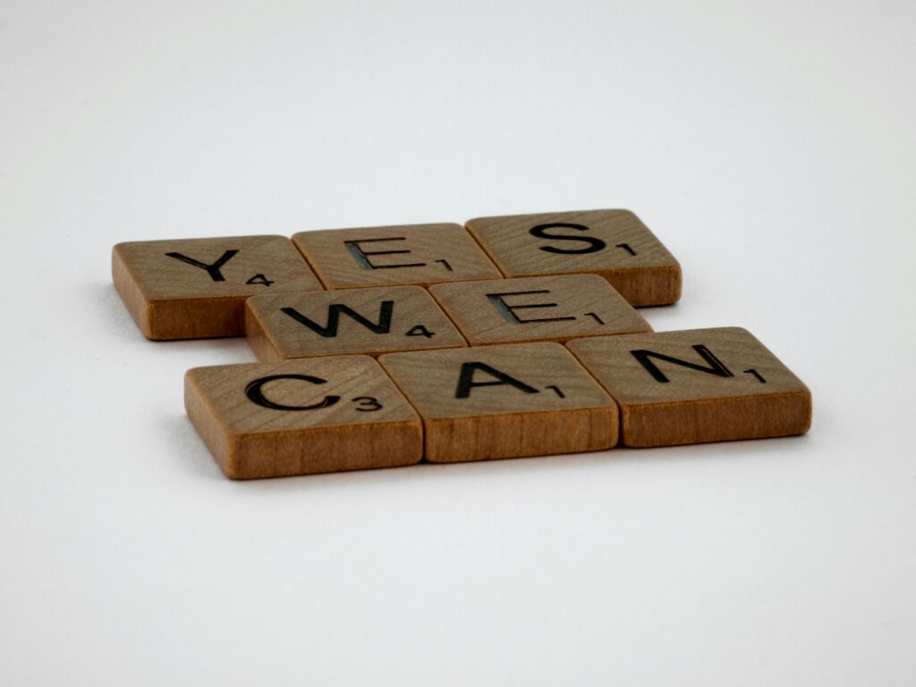 Scrabble tiles spelling 'Yes We Can' on a white background, conveying encouragement.